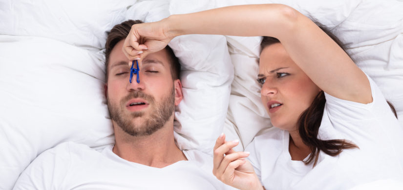 Frustrated Young Woman Trying To Stop Man's Snoring With Clothespin On Bed